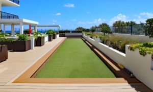 A modern rooftop terrace with multiple shaded seating areas, long planters, and a strip of artificial turf in the middle.