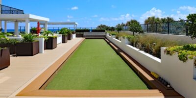 A modern rooftop terrace with multiple shaded seating areas, long planters, and a strip of artificial turf in the middle.