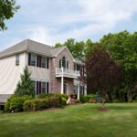 A large New England-style residential home, complete with a sprawling and well-maintained front lawn.