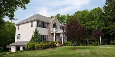 A large New England-style residential home, complete with a sprawling and well-maintained front lawn.