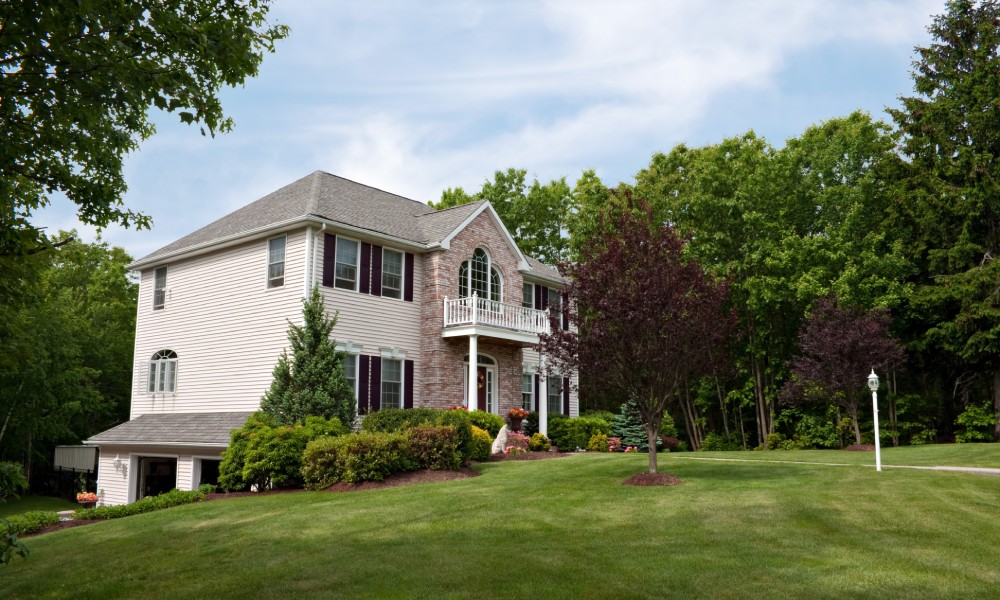 A large New England-style residential home, complete with a sprawling and well-maintained front lawn.