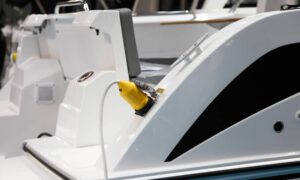 A white electric boat sits in the marina, receiving an electric charge from a bright yellow charger.