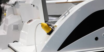 A white electric boat sits in the marina, receiving an electric charge from a bright yellow charger.