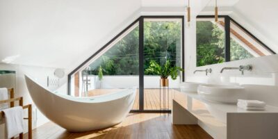 A clean, airy bathroom with a freestanding bathtub and a floor-to-ceiling window leading to a deck or patio.