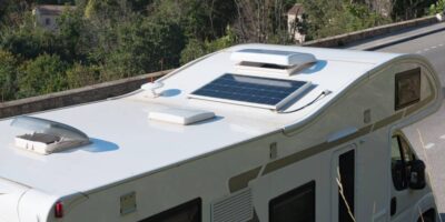 An overhead view of an RV parked on a roadway in full sun. The RV's roof has a solar panel and the RV roof vents are open.