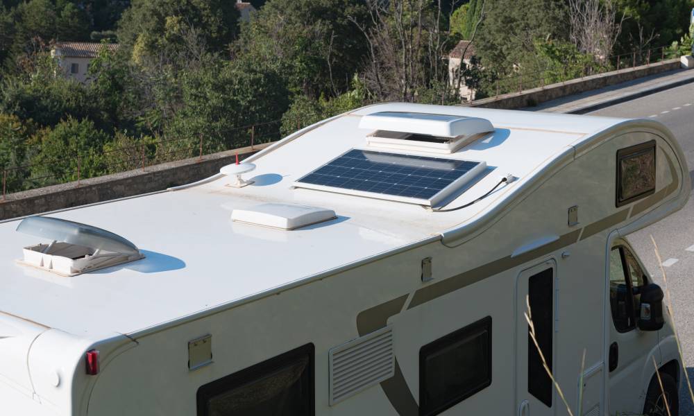 An overhead view of an RV parked on a roadway in full sun. The RV's roof has a solar panel and the RV roof vents are open.