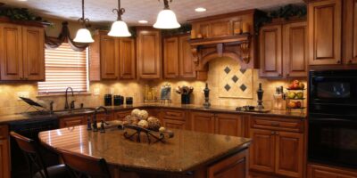 An expensive-looking Tuscan-style kitchen with dark cabinets and countertops, black appliances, and an intricate tile backsplash.