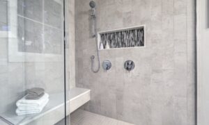 A gray-tiled walk-in shower contains a bench with a white towel and a gray washcloth. There's a window in the shower.