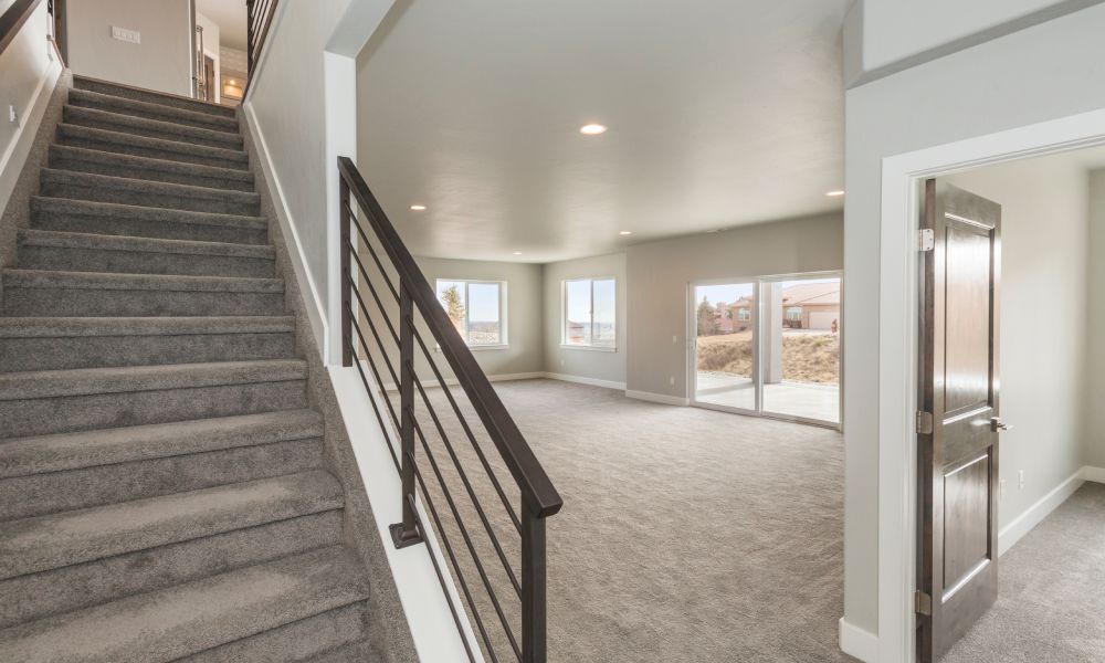 A carpeted staircase that leads down into a beautiful, open-concept basement with recessed overhead lighting.