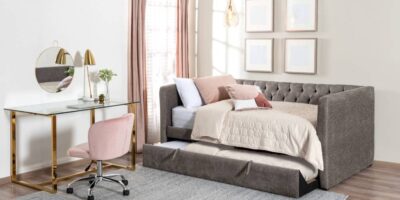 A room with an office desk and a day bed near the window. The furniture has a soft tone color of pink, white, tan, and gray.