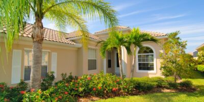 On a bright, sunny day, a home is nestled in a peaceful yard with lush, tropical trees and a green garden.