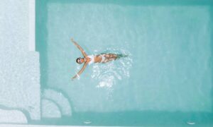 An overview of a woman wearing a white bathing suit set, relaxing in clear pool water on a hot, sunny day.