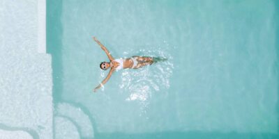 An overview of a woman wearing a white bathing suit set, relaxing in clear pool water on a hot, sunny day.