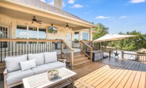 A backyard deck with a wooden table and a couch with gray cushions. It is a bright, partly cloudy day.