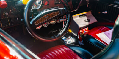 Interior view of a vehicle's front seat. The vehicle has red leather seats, a black steering wheel, and a cooler in passenger's seat.