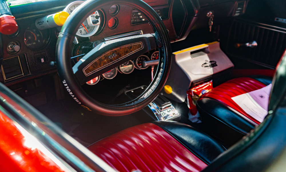 Interior view of a vehicle's front seat. The vehicle has red leather seats, a black steering wheel, and a cooler in passenger's seat.