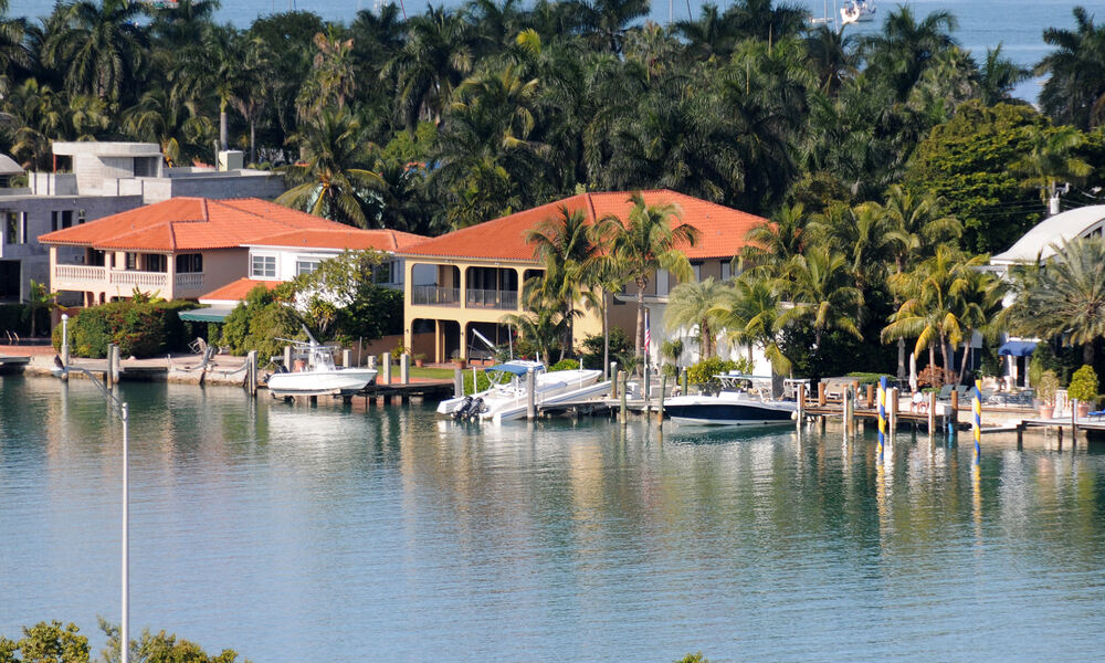 A neighborhood of luxury waterfront homes with palm trees in the homes' backyards, and boat docks in their front yards.