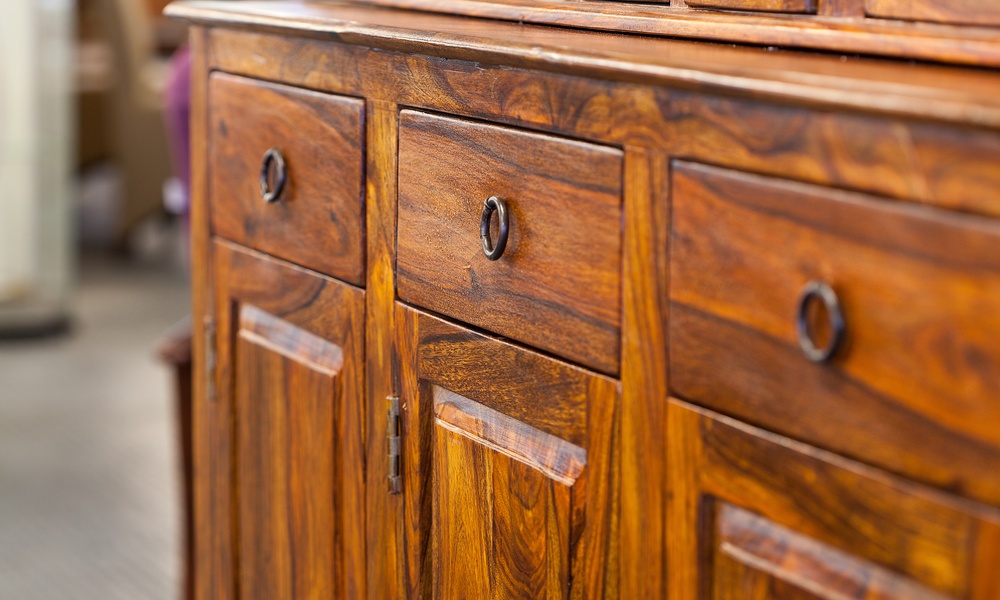 An antique wooden stand with three cabinets beneath three rectangular drawers. It features dark metal hinges and handles.